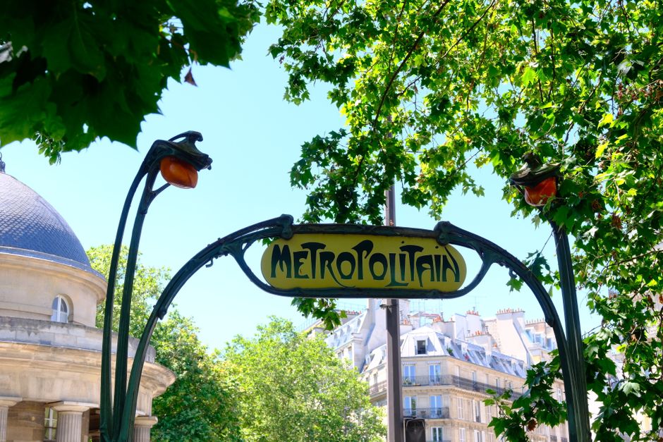 Parisian metro entrance sign with Art Nouveau style surrounded by lush greenery.