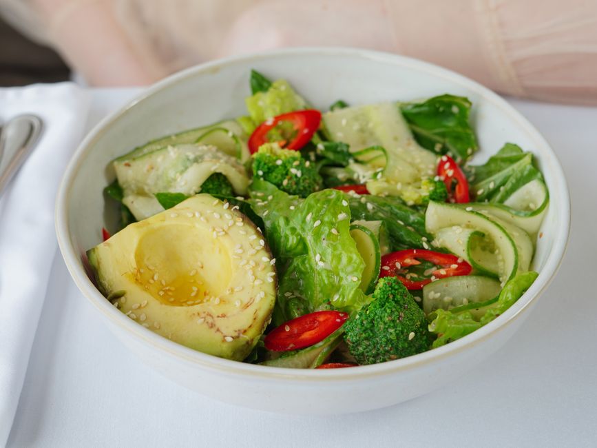 Colorful bowl of fresh vegetable salad with avocado, cucumber, and broccoli topped with sesame seeds.